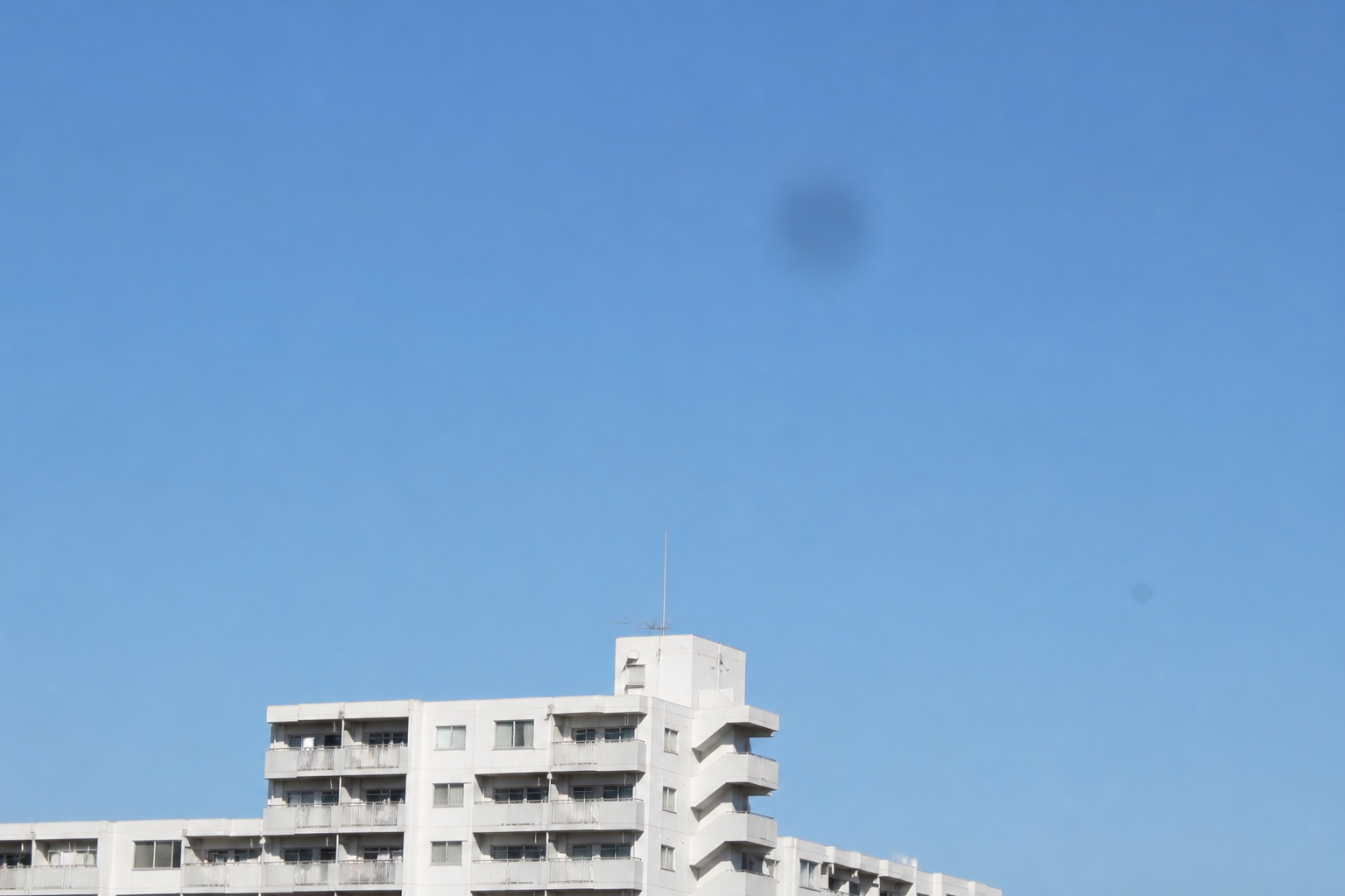 コンデジのセンサーゴミがズーム時に空へ影のように写り込んだ例