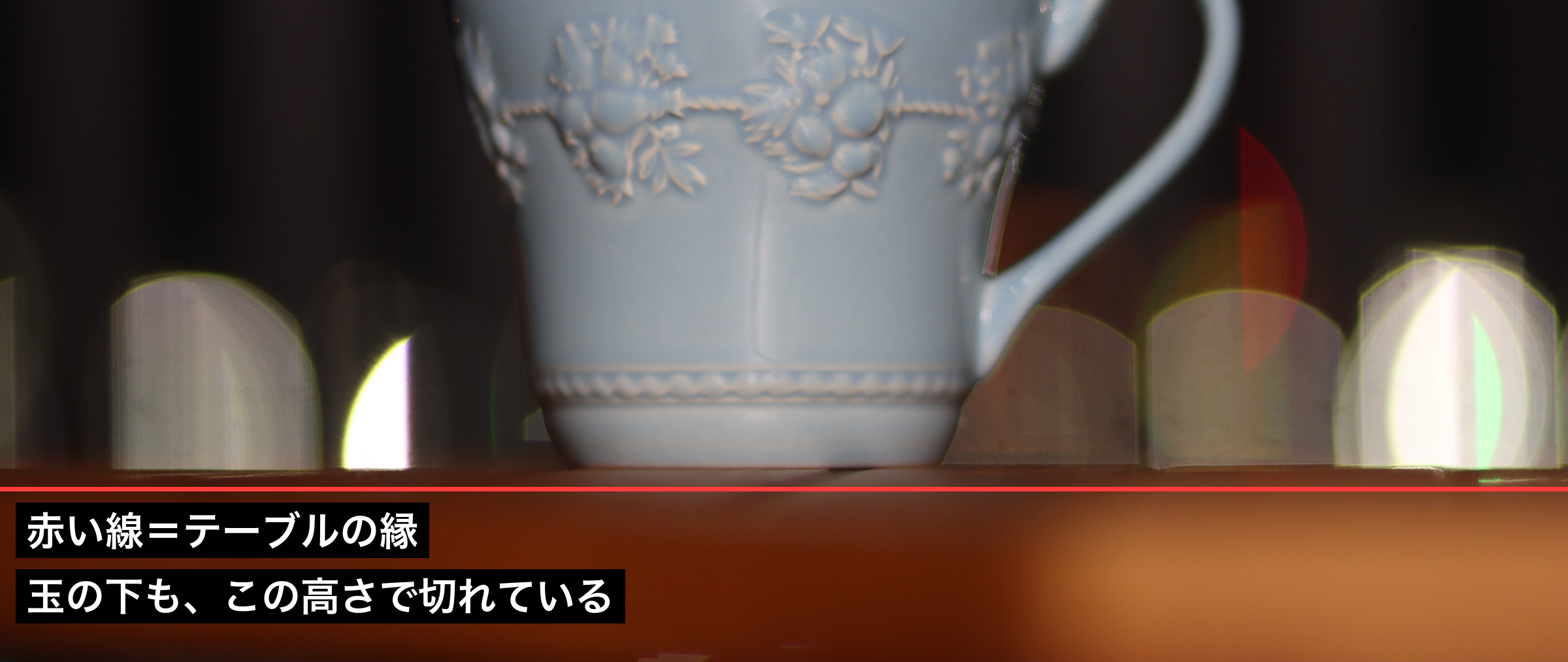 IMG_0044の玉ボケにテーブルの奥の縁の高さで赤い線を引いた図。玉の下の辺が線と同じ高さで切れている
