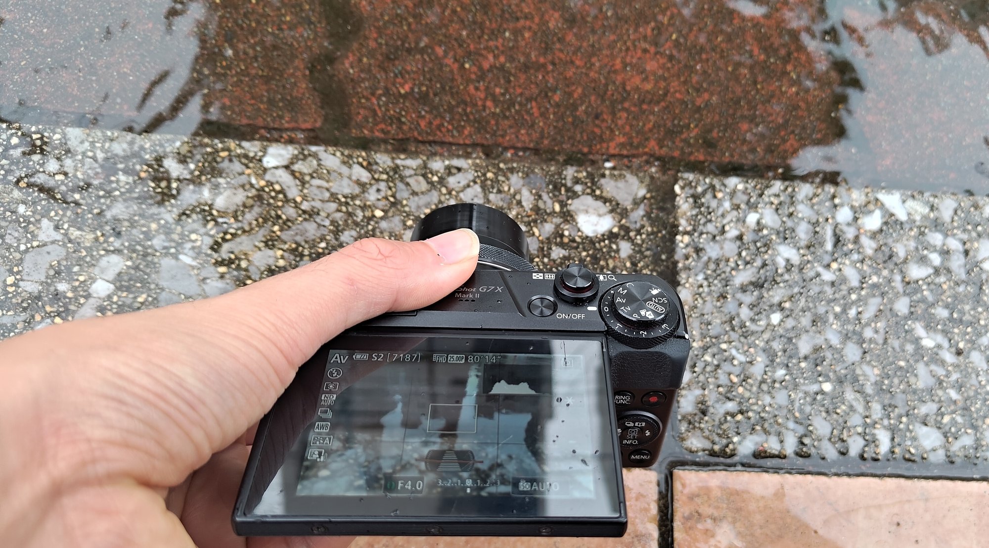 路面すれすれで構えたPowerShot G7X Mark II。上に開いた液晶にAv・F4.0・ISO AUTOの表示
