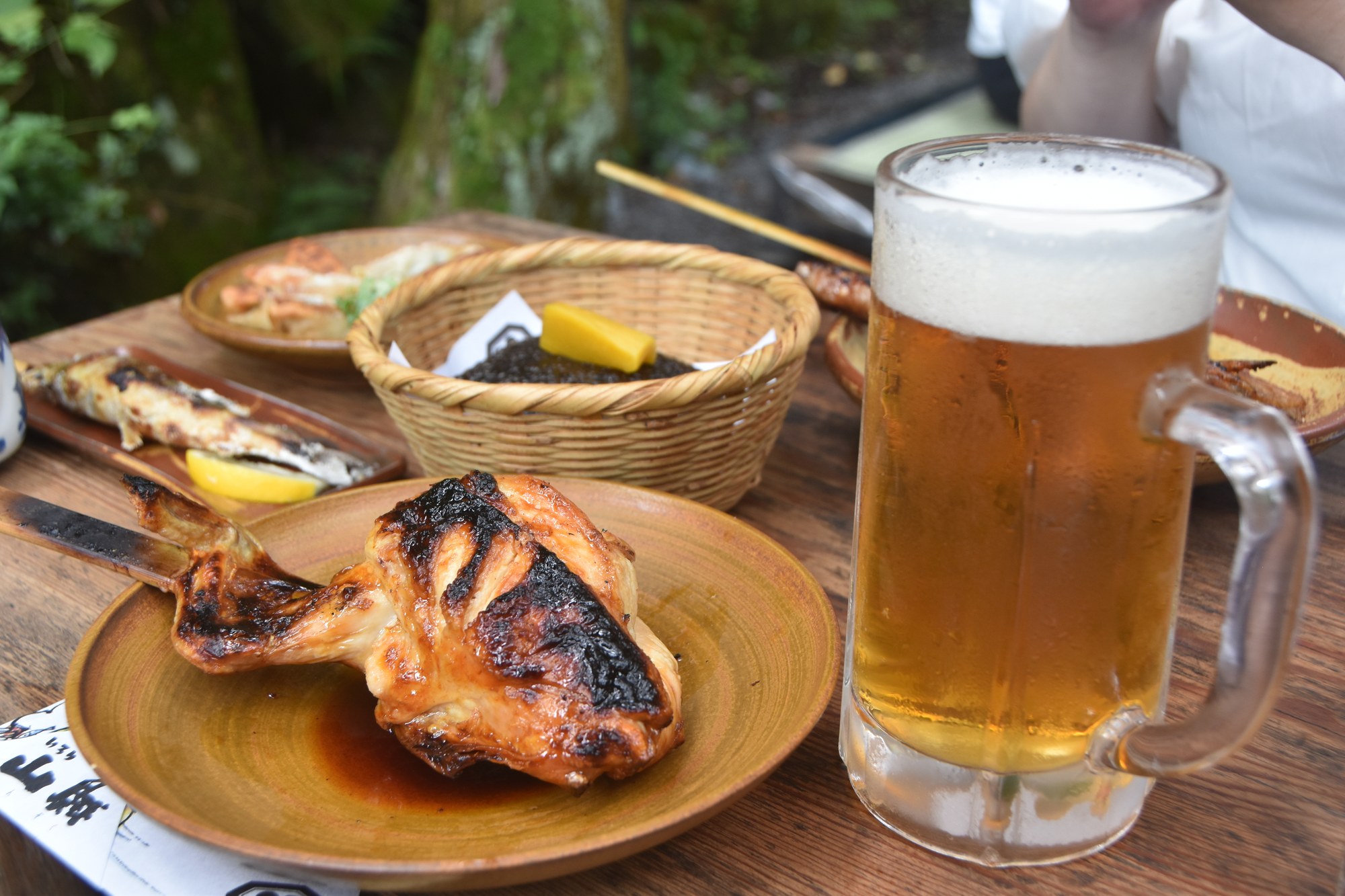 いろり山賊の山賊焼と生ビール。露出補正0でタレの照りと焼き目の焦げが写っている