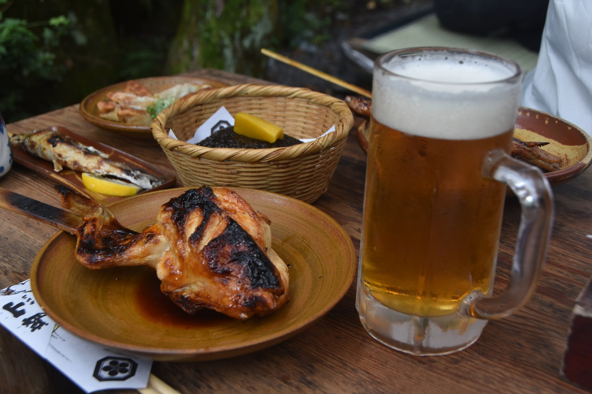 いろり山賊の山賊焼と生ビール。露出補正−1でテーブルと皿の色が沈んで暗い