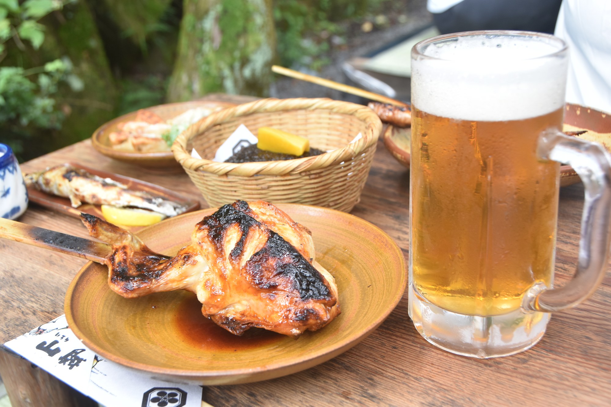 いろり山賊の山賊焼と生ビール。露出補正+1でビールの泡が白飛びしている