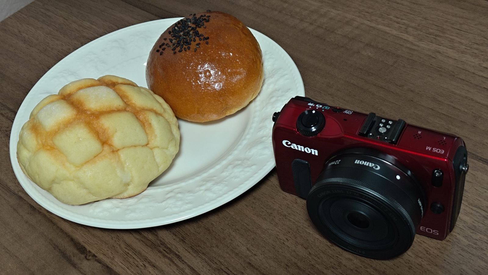 赤いCanon EOS Mと、メロンパン・あんパンをのせた皿