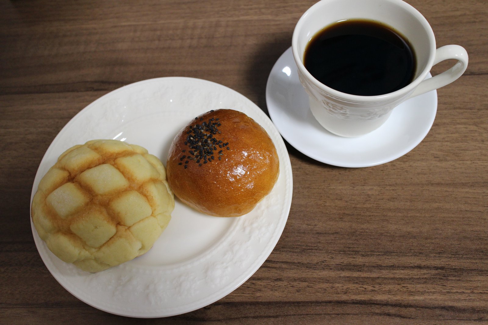 白い皿のメロンパンとあんパン、右奥にコーヒーカップが入った全景