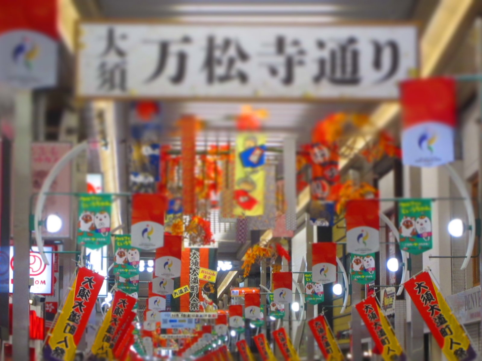 万松寺通りの入口の看板と、通りの両側に並ぶのぼり旗。ジオラマ風でのぼり旗のあたりがくっきりし、看板と天井がぼけている