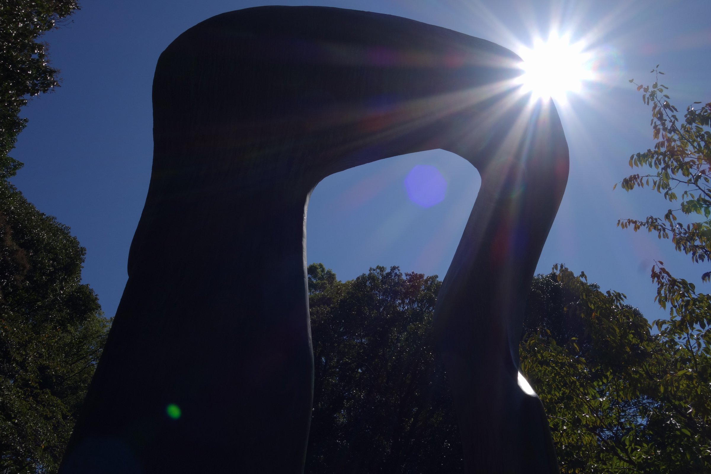 黒い影になったアーチの彫刻と濃い青空。梁の右端の角から太陽がのぞき、星のような形の光が出ている