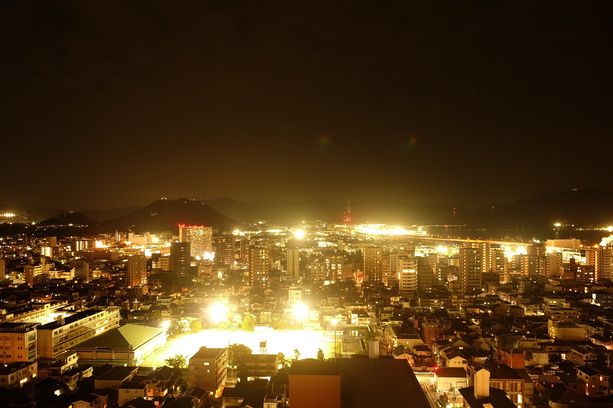 街全体が金色っぽく写った夜景。空は暗い茶色で、グラウンドが黄色っぽい白に光っている
