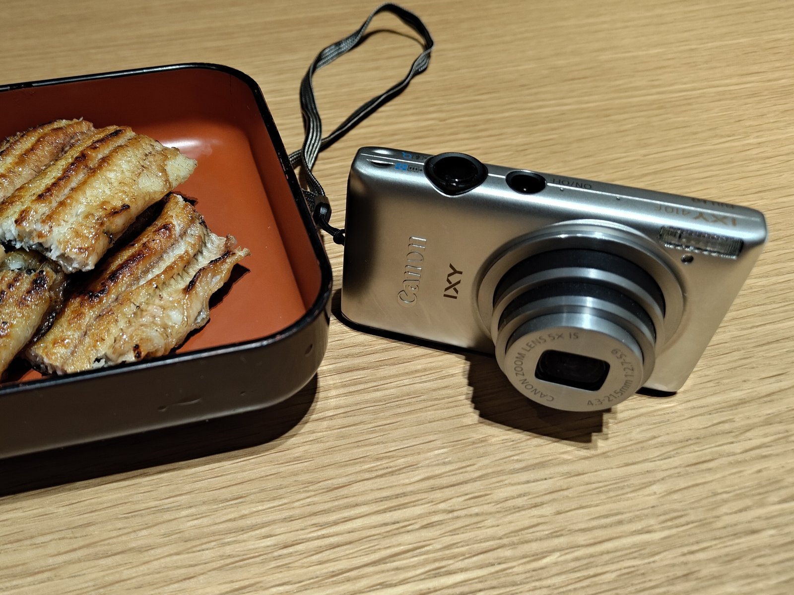 鰻の白焼きの横に置いた、銀色のCanon IXY 410F
