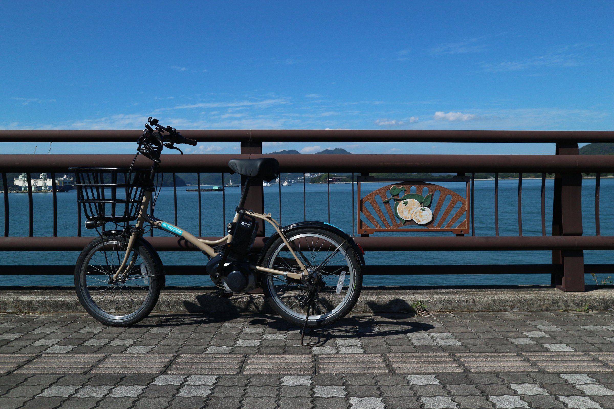 みかんのレリーフがある柵の前に停めたレンタサイクルと、真っ青な海